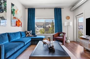 Living room with a blue couch, large window with curtain and table